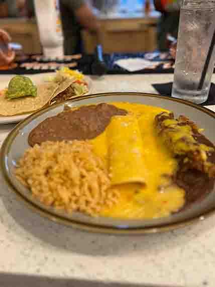 Number 2 platter featuring a cheese enchilada with Chile con Carne, a cheese enchilada with Queso, a crispy beef taco, and a guacamole tostada, a flavorful Tex-Mex combination at Tequileros restaurant in Frisco, Collin County, Texas.